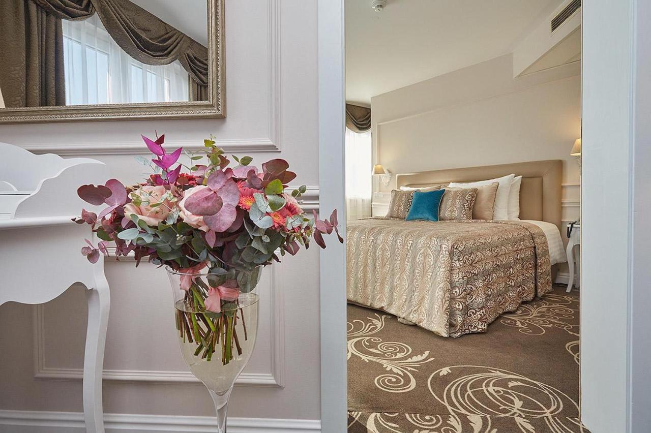 Don Giovanni Hotel Prague - Great Hotels Of The World Esterno foto The photo shows an inviting interior space that includes a well-decorated bedroom and a stylish floral arrangement. On the left side, there’s a tall vase containing colorful flowers, featuring shades of pink and green. The vase is situated on a white