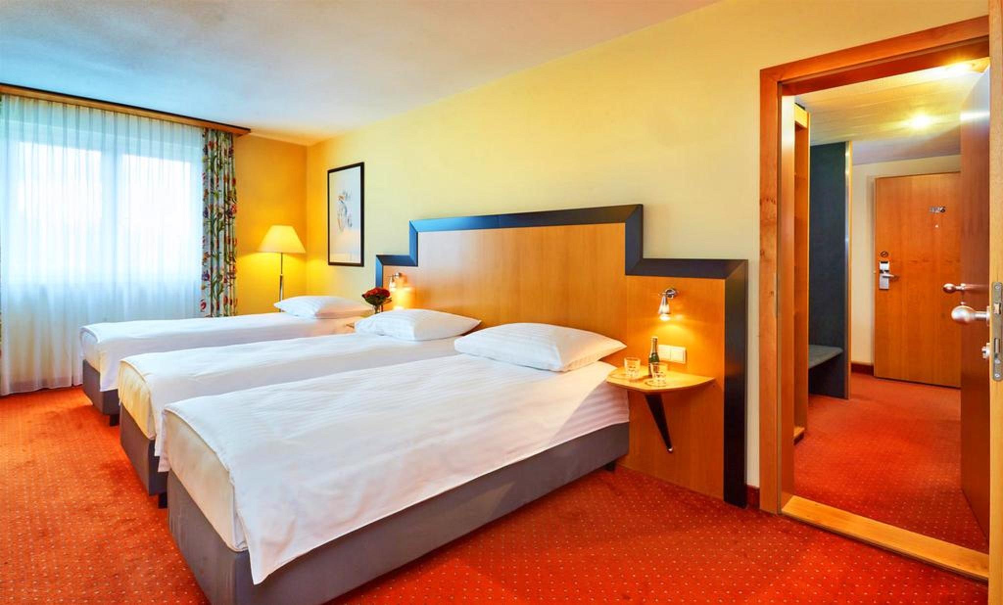 Don Giovanni Hotel Prague - Great Hotels Of The World Esterno foto The photo shows a brightly lit hotel room featuring three single beds with white bedding and gray bases. The walls are painted a warm yellow, and there are decorative curtains on the window, allowing natural light to enter. A bedside table is next to