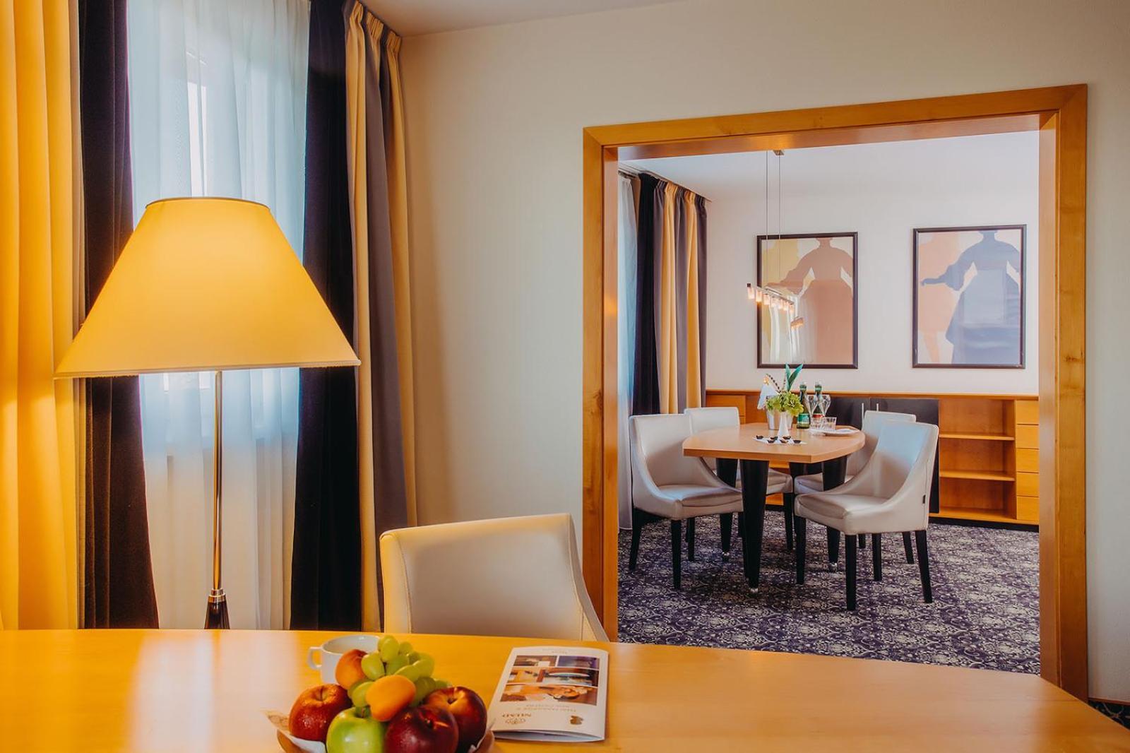 Don Giovanni Hotel Prague - Great Hotels Of The World Esterno foto The photo shows a well-decorated interior space, likely a hotel room or a suite. In the foreground, there is a wooden table with a bowl of colorful fruits and a magazine resting on the surface. A modern lamp stands beside the table, providing soft li